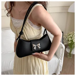 Detail of a black underarm bag featuring a silver metal bow buckle and knotted shoulder strap