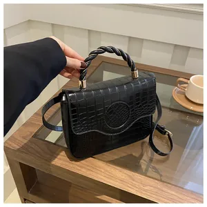 Detail of black crocodile texture handbag with twisted handle and golden hardware