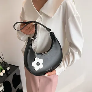 Minimalist black crescent shoulder bag with silver zippers and a white flower pendant