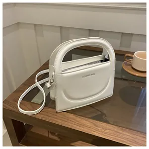 Detail of white leather handbag with curved handle and FASHION & BAGS logo on a table