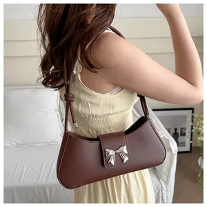 Detail of dark brown leather underarm bag featuring a silver metal bow buckle accent
