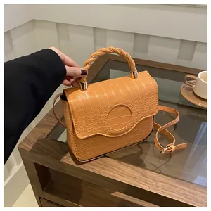 Detail of orange crocodile pattern handbag with twisted woven handle and side strap
