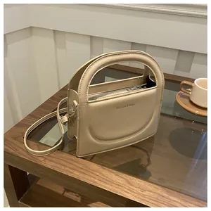 Detail of beige leather crossbody bag with semi-circular handle and embossed text