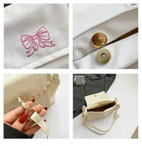Détails de broderie papillon et boucle dorée sur un sac bandoulière blanc cassé