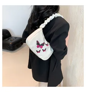Detail of a creamy white shoulder bag featuring pink butterfly embroidery and pleated strap