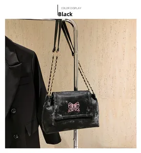 Détail du sac bandoulière noir avec broderie papillon rose et chaîne dorée