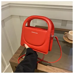 Detail of red PU leather small square bag with white Fashion & Bags text on wood table