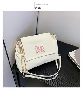Détail du sac blanc avec broderie papillon, plis souples et bandoulière dorée