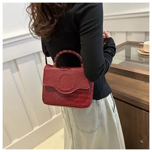 Detail of red crocodile texture handbag with spiral handle and wavy flap closure