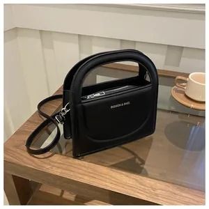 Detail view of the black leather textured small square bag with white lettering and handle