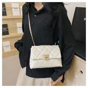 Detail of white quilted crossbody bag with gold buckle and chain strap on shoulder