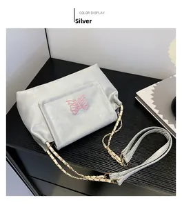 Détail du sac argenté avec broderie papillon rose et bandoulière en chaîne métal