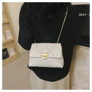 Detail of cream quilted crossbody bag with gold chain strap on a model shoulder