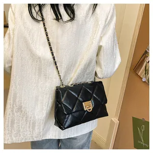Detail of black quilted crossbody bag with gold chain strap and metallic press-lock closure