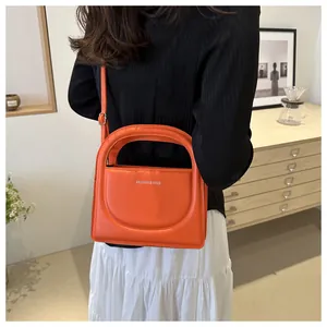 Detail of a bright orange mini handbag featuring a sleek semi-circular handle and smooth finish