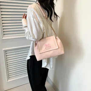Sac à bandoulière rose chic avec broderie papillon et chaîne dorée sur mannequin