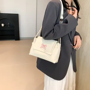 Sac à bandoulière crème avec broderie papillon rose et chaîne dorée sur mannequin