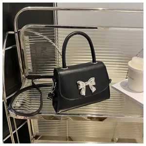 Detail of elegant black matte leather handbag featuring a silver metal bow ornament