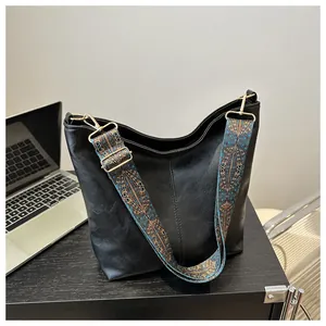 Detail of black leather tote bag featuring a colorful ethnic style wide fabric shoulder strap