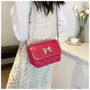 Detail of rose red quilted crossbody bag featuring a silver metal bow and gold trim