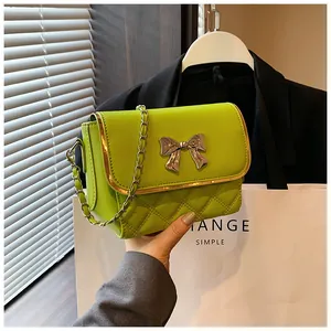Detail of green quilted crossbody bag with golden bow ornament and chain strap