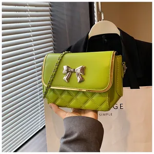 Detail of bright green quilted crossbody bag with silver bow and metal chain strap