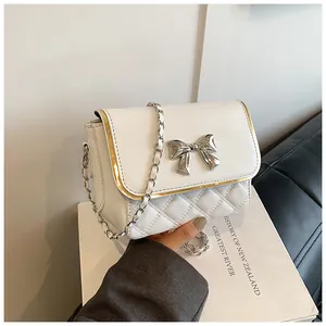 Detail of white quilted leather bag with metallic bow accent and gold-trimmed edge