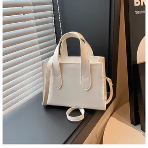 Detail of a minimalist cream square handbag with decorative stitching and twin handles