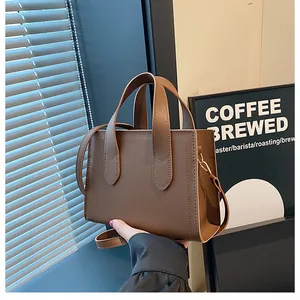 Detailed view of a brown box-shaped handbag with textured leather and gold hardware
