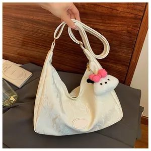 Detail of white glossy pleated hobo bag with a plush puppy charm on a wooden backdrop