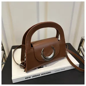 Detail of a brown leather handbag featuring a large silver crescent metal buckle on the flap