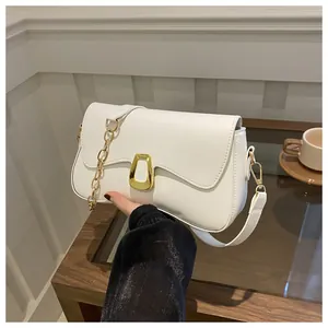 Detail of white leather shoulder bag with gold metal clasp and chain on a wooden table