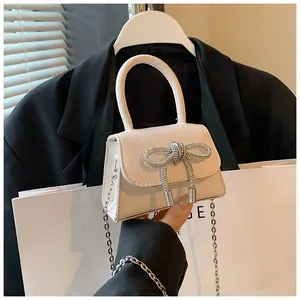 Detail van een witte lederen handtas met een glanzende strik van strass en zilveren ketting