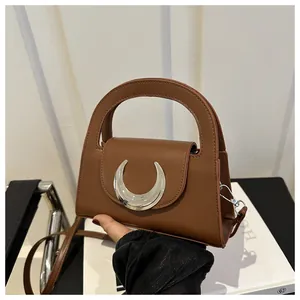Detail of caramel leather handbag featuring a crescent silver buckle and semi-circle handle