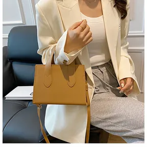 Close-up of brown leather handbag with handle and strap worn by a model in a suit