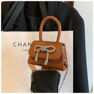 Detail van bruine mini-tas met litchi-patroon en een grote sprankelende strass-strik