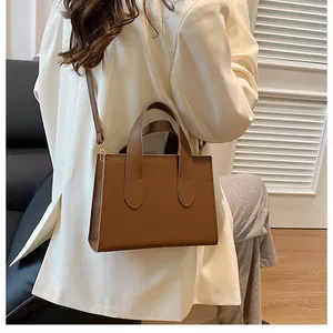 Brown leather tote bag worn crossbody by a model in a minimalist indoor setting