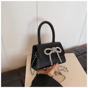 Detail van zwarte mini-tas met sprankelende strass-strik en een litchi-leer textuur look