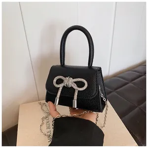 Detail van een zwarte mini-tas van kiezelleer met een glanzende strik van stras en ketting