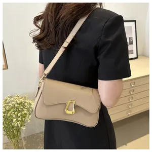 Detail view of khaki shoulder bag with wave flap and gold buckle worn on a black dress