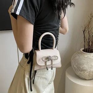 Elegante crème handtas met strass-strik en zilverkleurige schouderketting