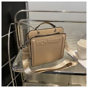 Close-up of beige crossbody bag showing Rich Rabbit embossed logo and woven strap