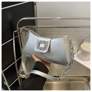 Detail of silver metallic shoulder bag featuring a sparkling rhinestone buckle and chain strap