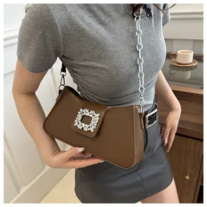 Detail of a brown shoulder bag featuring a crystal square buckle and silver chain strap