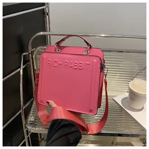 Detailed close-up of pink leather tote bag with embossed RICH RABBIT text and wide strap