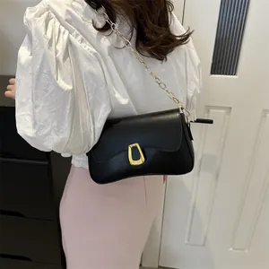 Minimalist black leather underarm bag with gold chain strap worn by a model