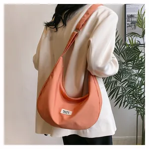 Detail view of the orange-pink canvas crossbody bag with branded label on a model