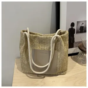 Detail of woven straw tote bag featuring leather logo patch and cotton rope handles