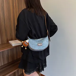 Blue denim moon bag with brown leather trim and plush charm worn by model