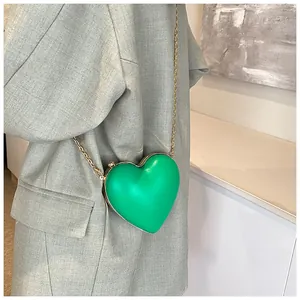 Detail of bright green heart-shaped crossbody bag with gold chain on grey blazer